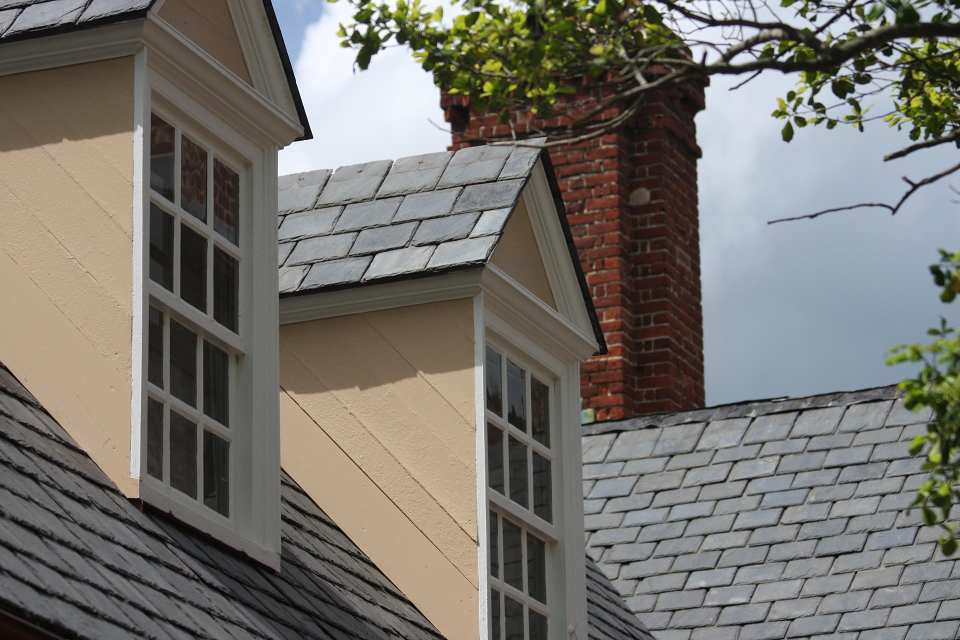 Natural slate roof featuring two dormer windows and a brick chimney on a classic home